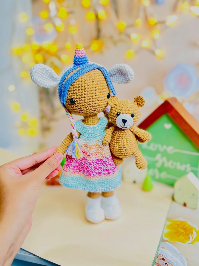 A hand-crocheted unicorn doll holding a small teddy bear